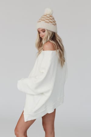 A woman wearing the Dana Oversized Diamond Texture Sweater in ivory stands against a plain light background, looking down with her shoulder exposed.