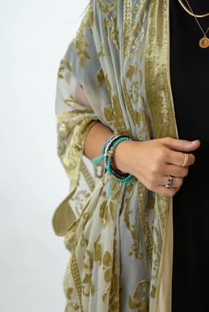 A person wears the Crushin' On You Velvet Kimono in olive over a black outfit, accessorized with layered turquoise bracelets, rings, and gold necklaces. Only the upper half of the body and one hand are visible.