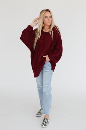 A woman with long blonde hair wears the Golden Hour Bubble Sleeve Sweater Dress in burgundy, standing against a plain white background.