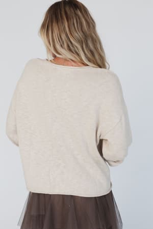 A woman with wavy blonde hair is shown from behind, wearing the Made You Smile Sweater in ivory and a dark sheer tulle skirt against a plain white background.