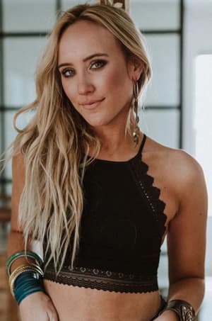 A woman with long blonde hair confidently poses indoors wearing the Light Of The Moon Crochet Trim Bralette in black, paired with large hoop earrings and colorful bangles.