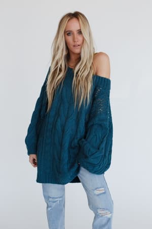 A woman with long blonde hair wears the Golden Hour Bubble Sleeve Sweater Dress in teal, styled off one shoulder, standing against a plain white background.