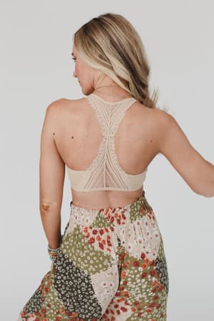 A blonde woman seen from the back wears the Evermore Seamless Lace Racerback Bralette in beige and a high-waisted green, red, and white floral skirt, standing against a plain light background.