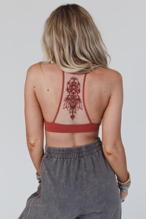 A woman with wavy blonde hair wears the Tattoo Bralette - Rust and gray pants, showcasing her back and a large, ornate temporary tattoo between her shoulder blades.