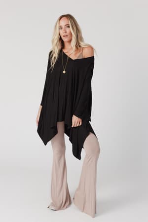 A woman with long blonde hair wears The Nest The Wren Top in black, featuring a flowy v-neckline, paired with beige flared pants and a gold necklace, standing against a plain white background.
