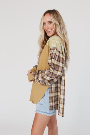 A woman with long blonde hair smiles in profile against a white background, wearing the Better Together Mixed Print Top - Mustard over a tan top and paired with light denim shorts.