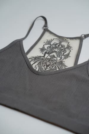 A close-up of the Tattoo Bralette - Gray showcases its sheer, embroidered mesh panel with intricate floral lace on the front, laid flat on a white surface.