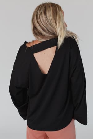 A person with long blond hair is seen from the back wearing The Nest Love It V Neckline Sweater Top in black and light pink pants, standing against a plain background.