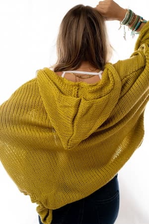 A person with long hair, seen from behind, wears the Cozy Hooded Cardigan - Mustard with dark jeans and colorful bracelets, standing against a white background.
