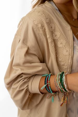 Wearing the Lorelei Crochet Jacket in beige, featuring embroidered and crochet details, paired with vibrant beaded bracelets. Only the lower face and upper body are shown.