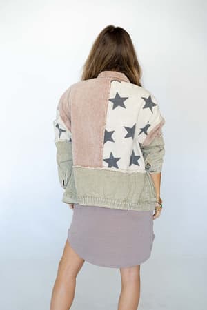 A woman with long brown hair faces away, wearing the Star Dust Contrast Corduroy Jacket - Multi with an oversized fit over a short mauve dress, standing against a plain white background.