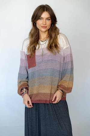 A woman with long, wavy brown hair wears the Going Places Gradient Stripe Sweater in mauve, featuring a chest pocket, paired with a dark skirt. She stands against a plain, light background and smiles softly at the camera.