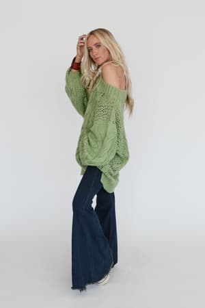 A woman with long blonde hair models the Golden Hour Bubble Sleeve Sweater Dress in light green, standing sideways and looking at the camera against a plain white background.
