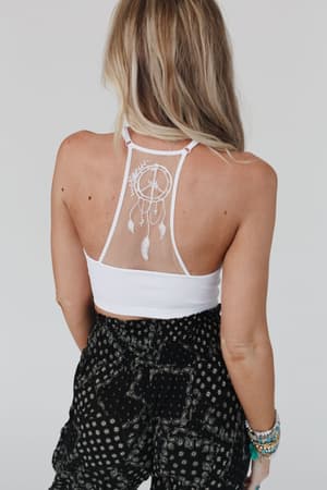 A woman with long blonde hair is shown from the back wearing a white Peace Dreamcatcher Tattoo Bralette and black patterned pants, accessorized with several beaded bracelets for a boho-inspired look.
