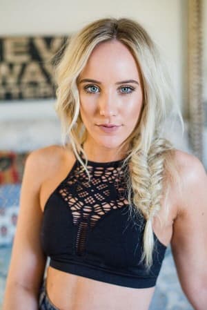 A woman with long blonde hair in a side braid wears the Floral Cut Out High Neck Bralette - Black, featuring a strappy back, and looks at the camera with a neutral expression. The background is softly blurred.