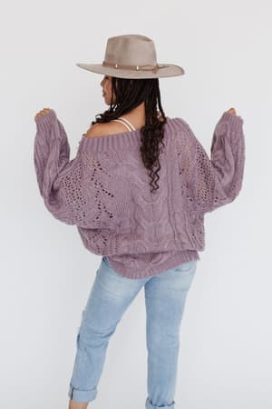 A person stands facing away against a plain white background, wearing braided hair, a beige hat, and the Golden Hour Bubble Sleeve Sweater Dress in Lavender with balloon sleeves and light blue jeans.