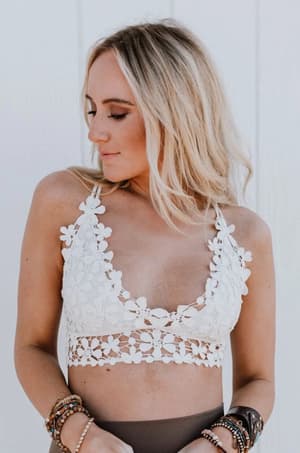 A woman with long blonde hair wears the Dainty Daisy Crochet Bralette - White and several beaded bracelets, looking down to her left against a plain white background.