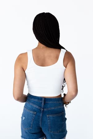 A woman with long braids stands with her back to the camera, wearing the Hook It Up Ribbed Brami in ivory and blue denim jeans against a plain white background.
