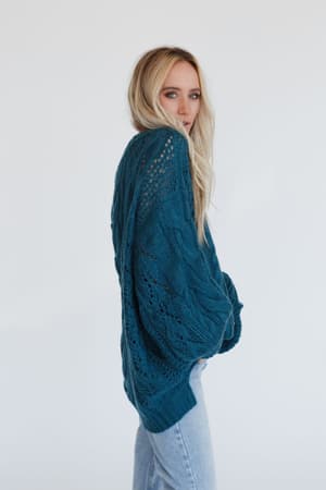 A woman with long blonde hair models the Golden Hour Bubble Sleeve Sweater Dress in teal, standing sideways and looking at the camera against a plain white background.