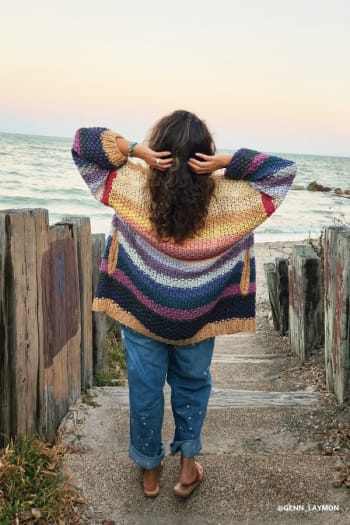 Person wearing a colorful striped sweater standing on a beach path.