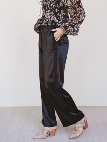 Person wearing a patterned top and black satin pants on a white background