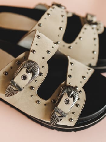 Close-up of a sandal with decorative straps and buckles on a pink background