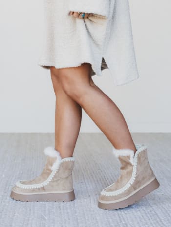 Person wearing beige winter boots with white fur trim on a light background