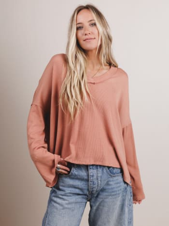 Woman wearing a peach long-sleeve top and blue jeans against a beige background