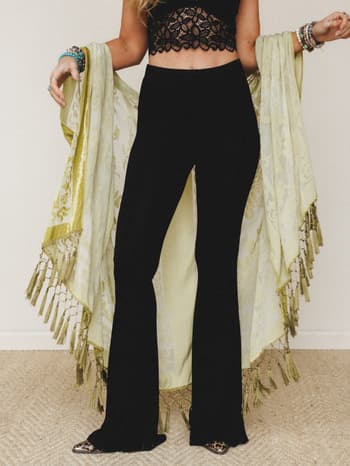 Black flare pants styled with a black lace crop top and a flowing sage green tassel kimono held open wide — the kind of outfit that's equally at home at a festival or a rooftop dinner.