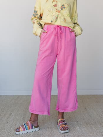 A cropped wide-leg pant in washed bubblegum pink styled with a butter yellow floral appliqué sweatshirt and multicolor platform sandals — playful, relaxed, and full of personality.