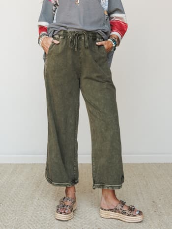 Wide-leg cropped pants in a washed olive with a relaxed drawstring waist, styled with a mixed-print top, stacked bead bracelets, and leopard platform sandals — the kind of outfit that looks intentional without trying too hard.