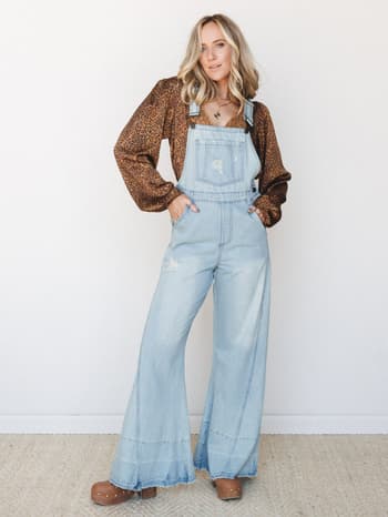Wide-leg denim overalls styled over a leopard print long-sleeve top with clogs and layered necklaces — that effortless 70s-meets-weekend energy that makes you want to immediately get dressed.