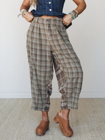 Pleated plaid trousers in earthy olive and brown tones styled with a cropped denim corset top, stacked bead bracelets, and wood-studded clogs — a laid-back vintage mix that feels effortlessly collected.