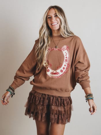Woman wearing a brown sweatshirt with a decorative horseshoe design and a matching skirt on a plain background