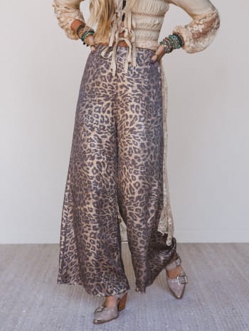 Person wearing leopard print pants and a light-colored top with ruffled sleeves against a neutral background