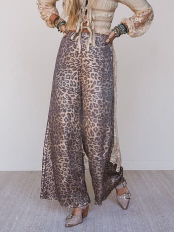 Person wearing leopard print pants and a light-colored top with ruffled sleeves against a neutral background