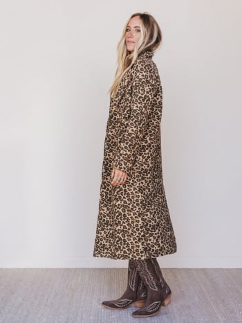 Woman wearing a leopard print coat and cowboy boots against a white background