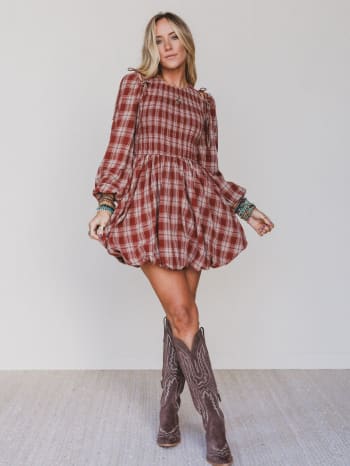 Woman wearing a plaid dress and cowboy boots against a plain background