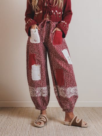 Person wearing a red sweater and patchwork pants on a plain background