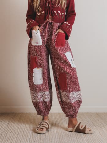 Person wearing a red sweater and patchwork pants on a plain background