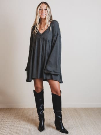 Woman wearing a dark gray dress and black knee-high boots indoors.