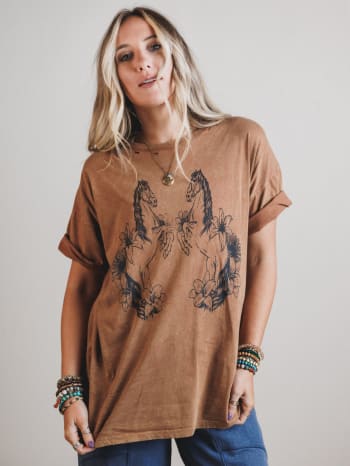 Woman wearing a brown t-shirt with horse and floral designs on a plain background