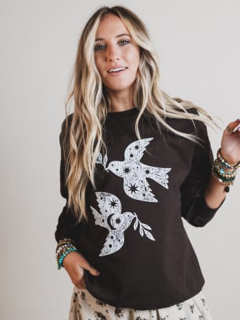 Woman wearing a black sweatshirt with white bird designs on a plain background