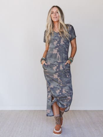 Woman wearing a camouflage dress with patterned socks and loafer mules against a plain background.