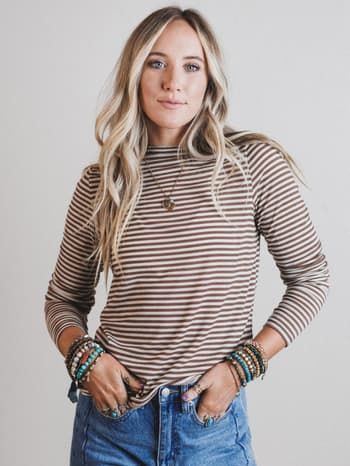 Woman wearing a striped long-sleeve shirt and jeans with bracelets on a plain background