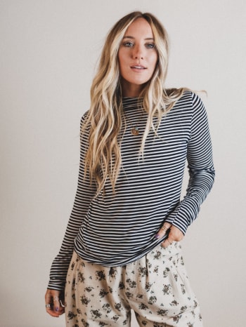 Woman wearing a striped long-sleeve top and floral pants against a plain background