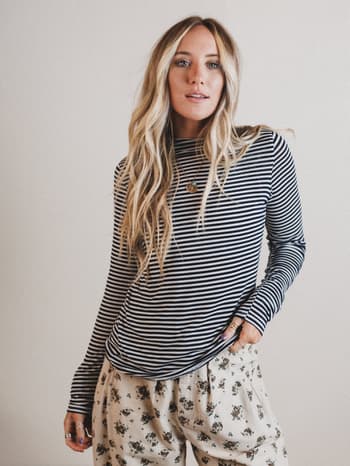 Woman wearing a striped long-sleeve top and floral pants against a plain background