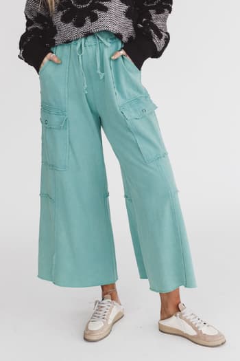 A person wearing green cargo wide leg pants with a drawstring waistband and multiple pockets, paired with a grey sweater and white sneakers.