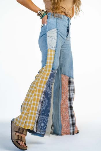 A person wearing Magnolia Patchwork Jeans - Washed Denim featuring mixed patterns and colors with a frayed hem, styled with sandals and layered bracelets.